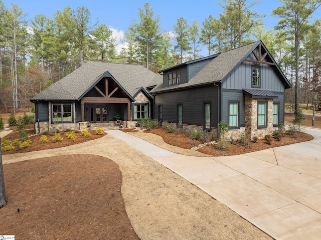 view of front of house with stone siding, french doors, concrete driveway, and roof with shingles