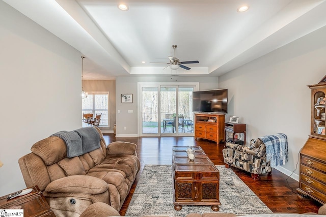 living room featuring baseboards, recessed lighting, dark wood-style flooring, ceiling fan, and a raised ceiling