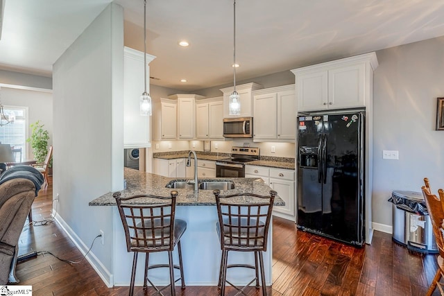 kitchen with dark wood-type flooring, dark stone countertops, a peninsula, stainless steel appliances, and a sink