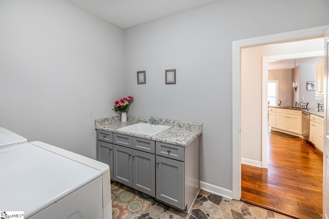 clothes washing area featuring independent washer and dryer, a sink, wood finished floors, cabinet space, and baseboards