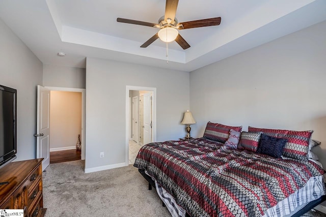 carpeted bedroom featuring baseboards, a raised ceiling, and a ceiling fan