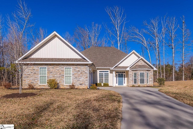 view of front facade featuring board and batten siding, a front lawn, stone siding, and roof with shingles