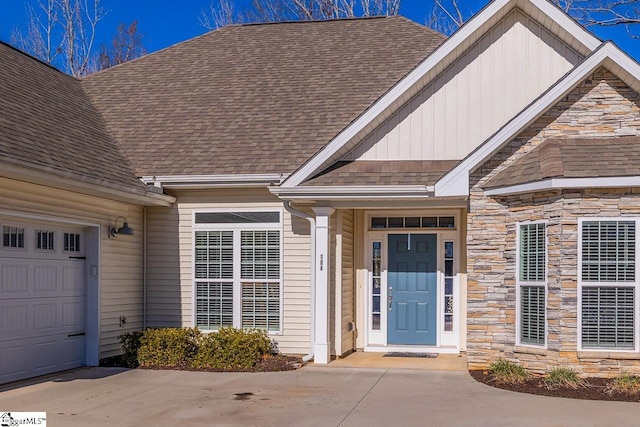 view of exterior entry featuring an attached garage, stone siding, and roof with shingles