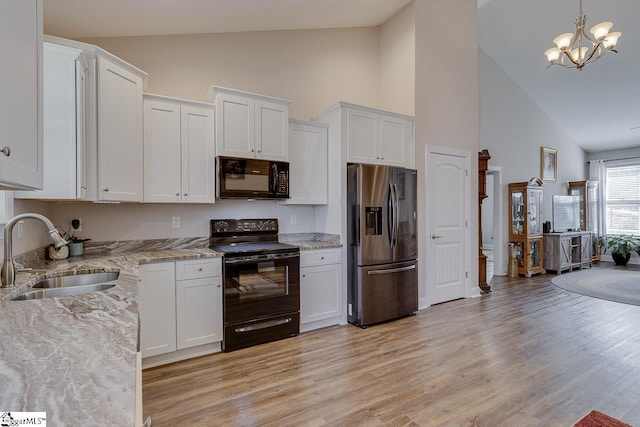 kitchen featuring light stone countertops, white cabinetry, black appliances, and a sink