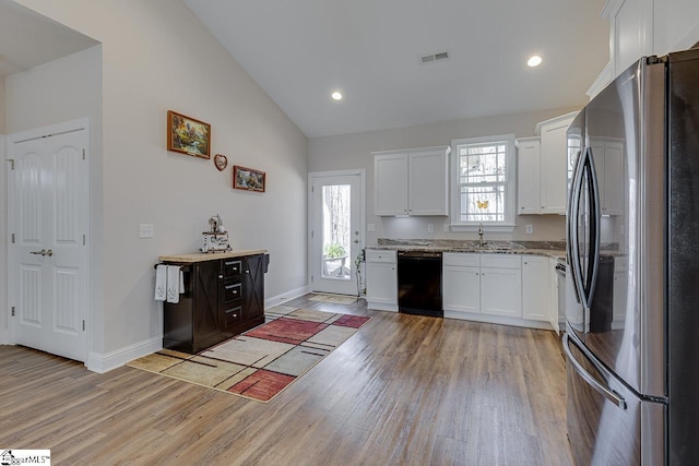 kitchen featuring visible vents, dishwasher, light stone counters, light wood-style flooring, and freestanding refrigerator