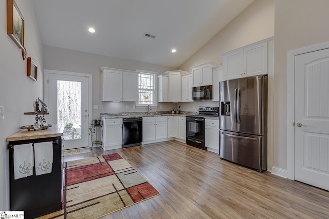 kitchen with visible vents, black appliances, white cabinetry, light wood finished floors, and light stone countertops