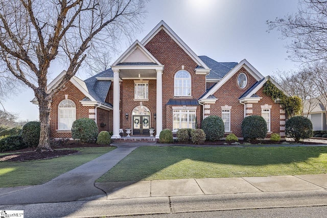 greek revival house with brick siding, french doors, a shingled roof, and a front yard