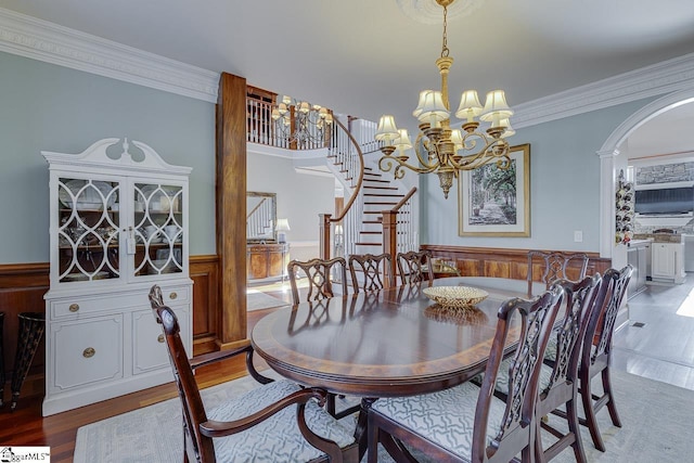 dining space featuring a wainscoted wall, wood finished floors, stairway, arched walkways, and a chandelier