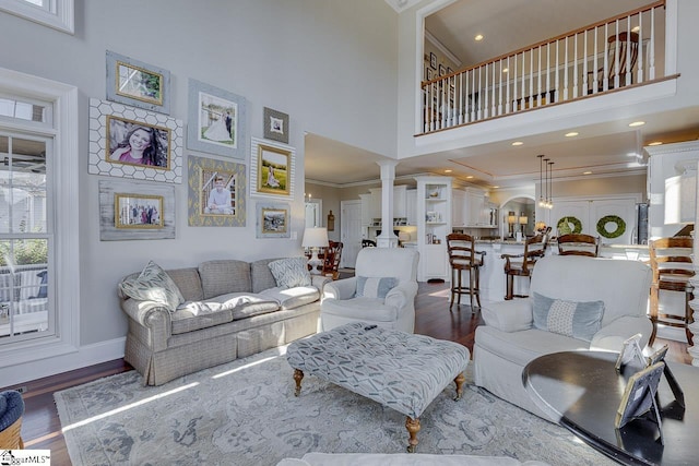 living room with wood finished floors, baseboards, ornate columns, a high ceiling, and ornamental molding