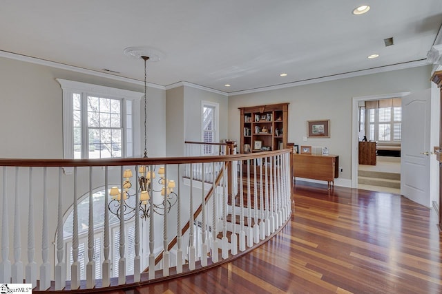 corridor featuring wood finished floors, baseboards, recessed lighting, crown molding, and a chandelier