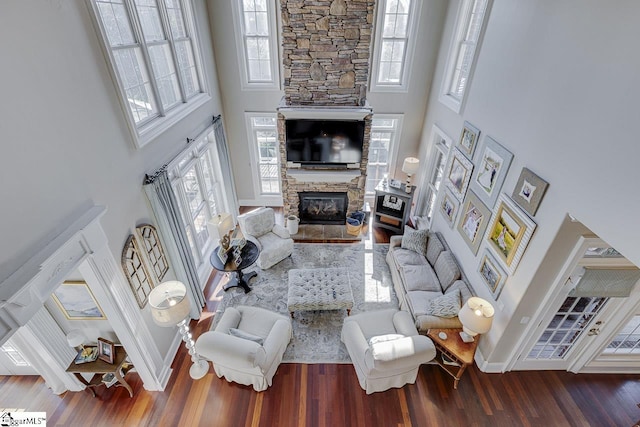 living room featuring plenty of natural light, a high ceiling, a stone fireplace, and wood finished floors