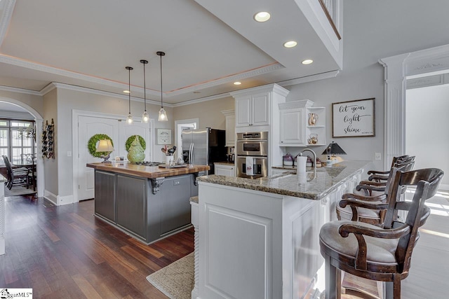 kitchen featuring wooden counters, a tray ceiling, arched walkways, a sink, and appliances with stainless steel finishes