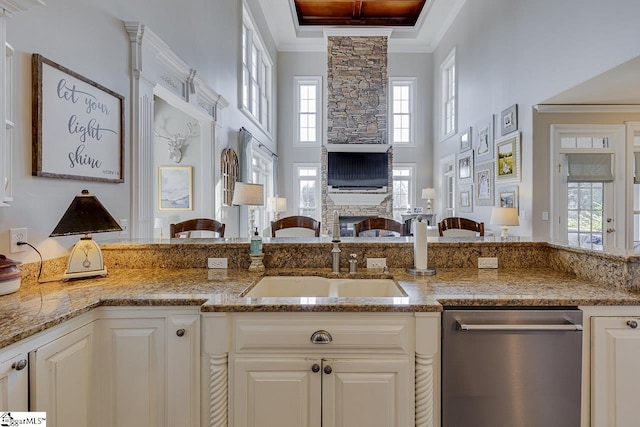 kitchen featuring ornamental molding, light stone counters, stainless steel dishwasher, open floor plan, and a fireplace