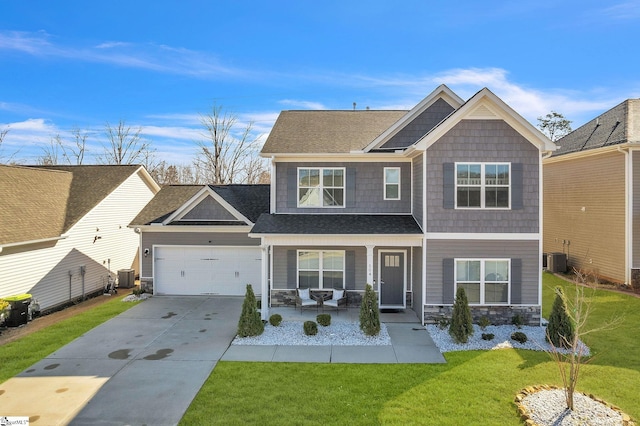 craftsman-style home featuring a front yard, central AC unit, covered porch, concrete driveway, and stone siding