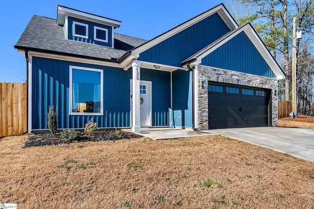 modern farmhouse style home with a front yard, fence, concrete driveway, a garage, and stone siding