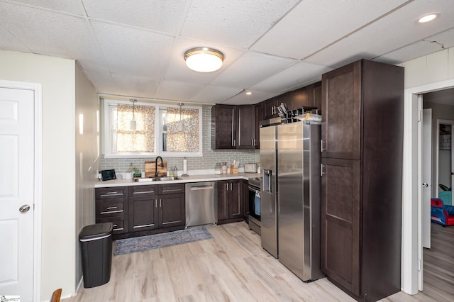 kitchen with a sink, stainless steel appliances, light countertops, light wood-style floors, and tasteful backsplash