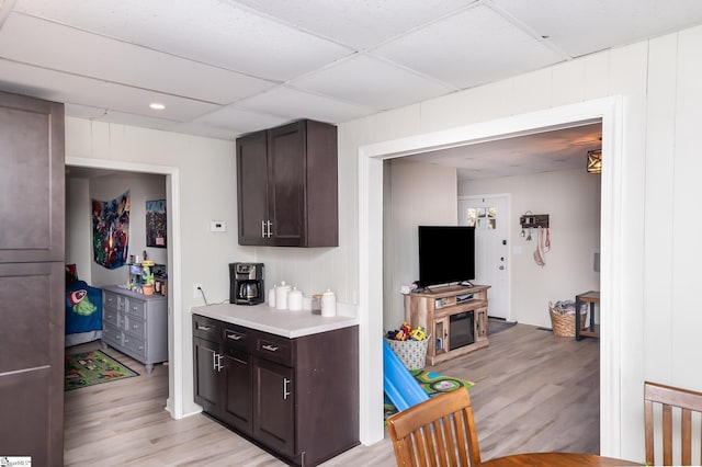 kitchen with light countertops, dark brown cabinets, a drop ceiling, and light wood finished floors