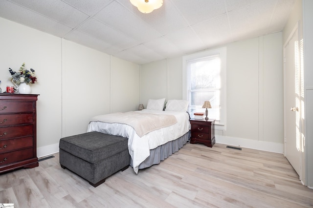 bedroom featuring visible vents, a paneled ceiling, baseboards, and light wood-style flooring