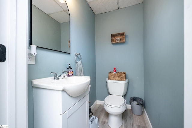 half bathroom featuring toilet, wood finished floors, a paneled ceiling, baseboards, and vanity