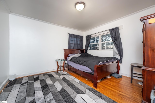 bedroom featuring baseboards, wood finished floors, and crown molding