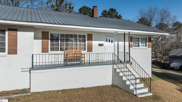 view of front of house featuring brick siding, a chimney, and metal roof