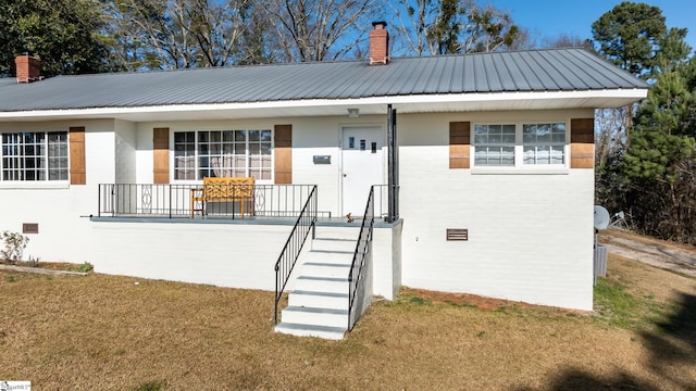 view of front facade with brick siding, a front yard, a chimney, metal roof, and crawl space