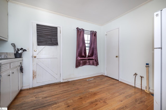 empty room featuring visible vents, light wood-type flooring, and ornamental molding