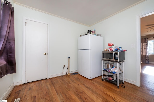 interior space with stainless steel microwave, wood finished floors, freestanding refrigerator, and ornamental molding