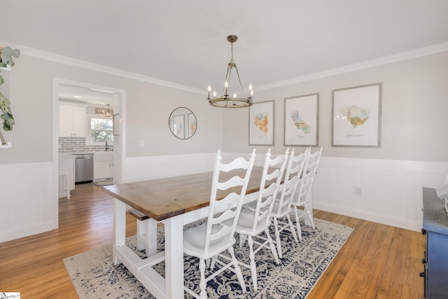 dining area with crown molding, light wood-type flooring, and an inviting chandelier