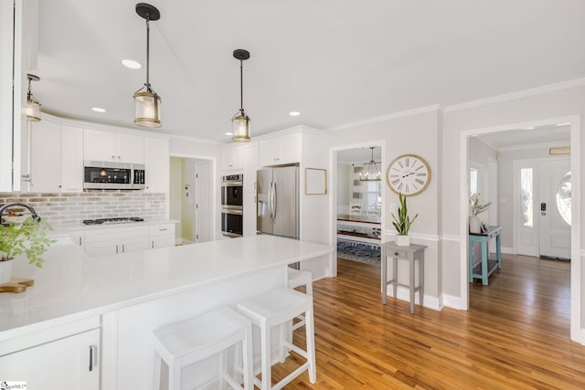 kitchen featuring light wood finished floors, a peninsula, stainless steel appliances, and ornamental molding