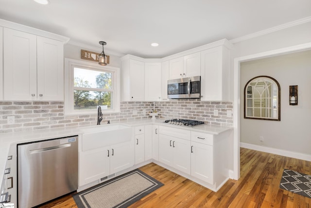 kitchen with appliances with stainless steel finishes, white cabinetry, light countertops, and a sink