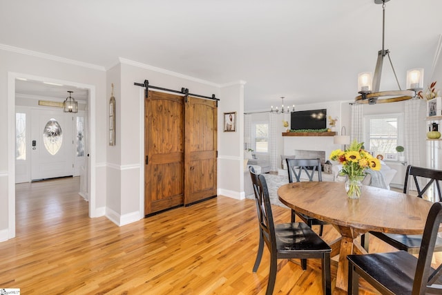 dining space with a barn door, a large fireplace, light wood-style flooring, and crown molding