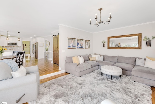 living room with an inviting chandelier, a barn door, crown molding, and light wood-type flooring