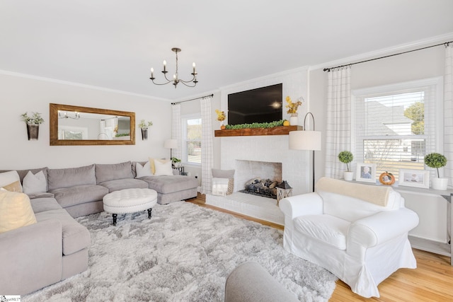 living room featuring a notable chandelier, a brick fireplace, wood finished floors, and crown molding