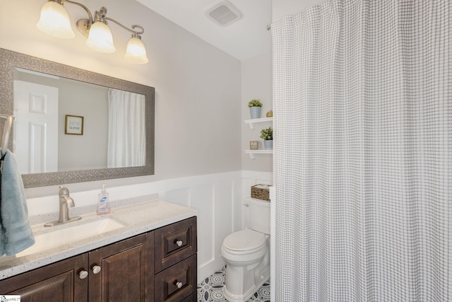 full bathroom with vanity, visible vents, wainscoting, a decorative wall, and toilet