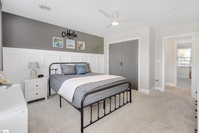 bedroom featuring ceiling fan, a closet, light colored carpet, and a wainscoted wall