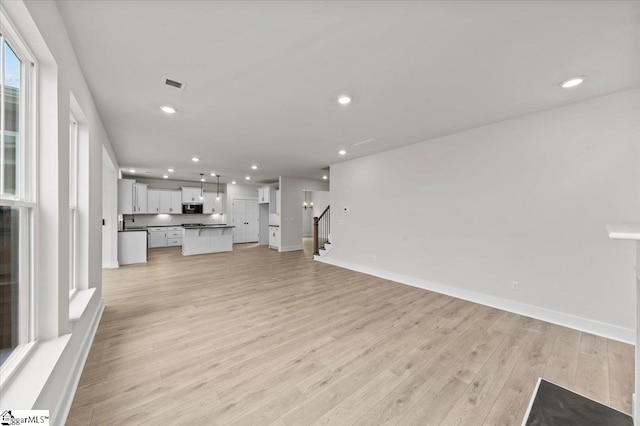 unfurnished living room featuring visible vents, baseboards, light wood-style flooring, recessed lighting, and stairs