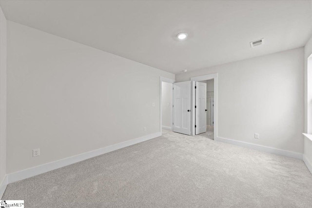 empty room featuring light colored carpet, visible vents, and baseboards