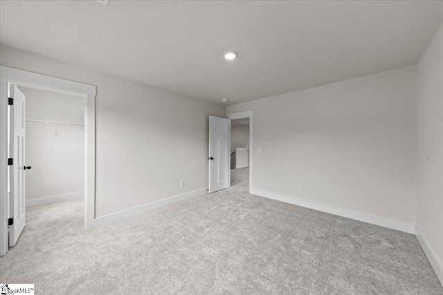 unfurnished bedroom featuring a spacious closet, light colored carpet, baseboards, and a closet