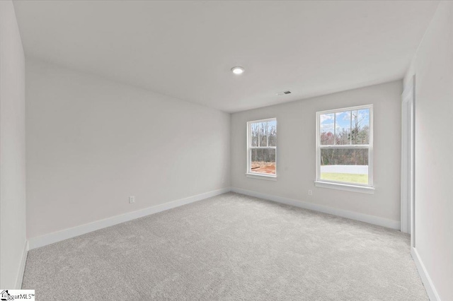 spare room featuring light colored carpet, visible vents, and baseboards