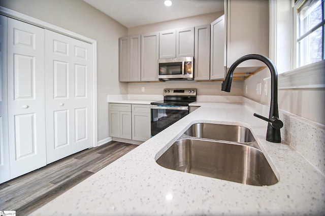 kitchen featuring a sink, light stone counters, dark wood-type flooring, and appliances with stainless steel finishes