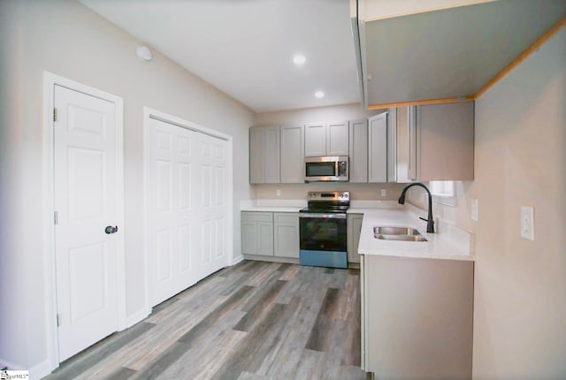 kitchen with gray cabinets, stainless steel appliances, light countertops, and a sink