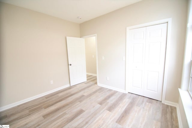 unfurnished bedroom featuring a closet, baseboards, and light wood-style flooring