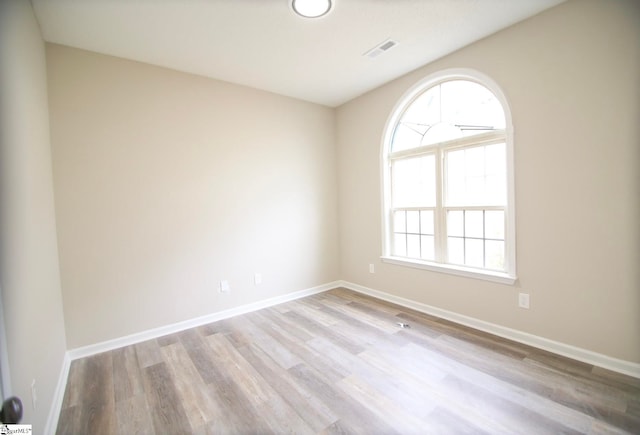 unfurnished room featuring wood finished floors, visible vents, and baseboards