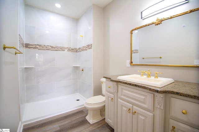 bathroom with vanity, toilet, wood finished floors, and tiled shower