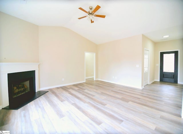 unfurnished living room with light wood finished floors, a fireplace with raised hearth, baseboards, and vaulted ceiling