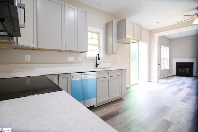 kitchen featuring a ceiling fan, light wood-style flooring, a fireplace, a sink, and dishwasher