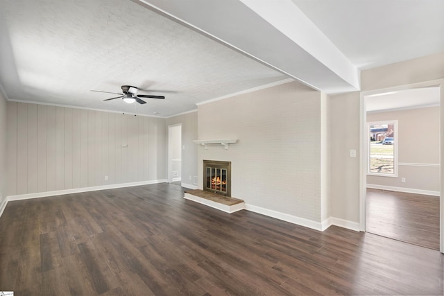 unfurnished living room with baseboards, dark wood finished floors, ornamental molding, a fireplace, and a ceiling fan