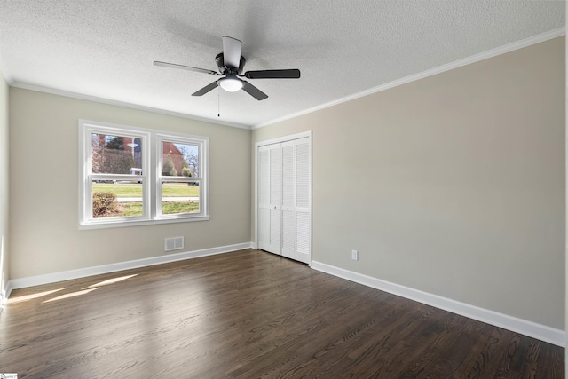 unfurnished bedroom with baseboards, visible vents, dark wood-style flooring, ornamental molding, and a closet