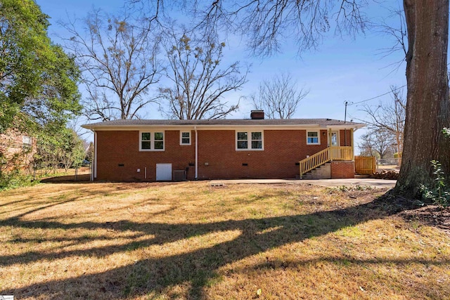 back of house featuring crawl space, brick siding, a chimney, and a lawn